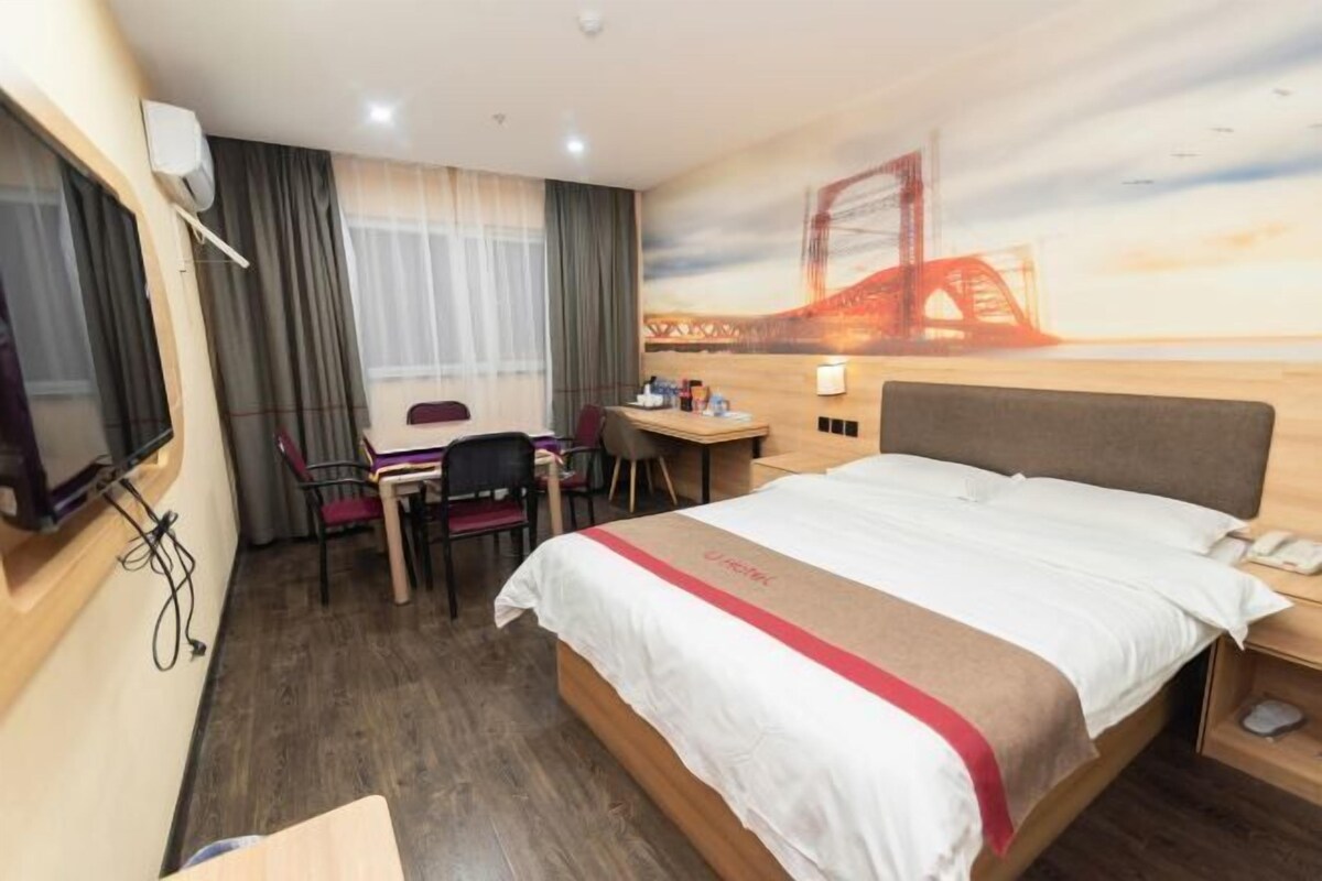 A hotel room with a bed, desk, chair, and a large window with curtains.