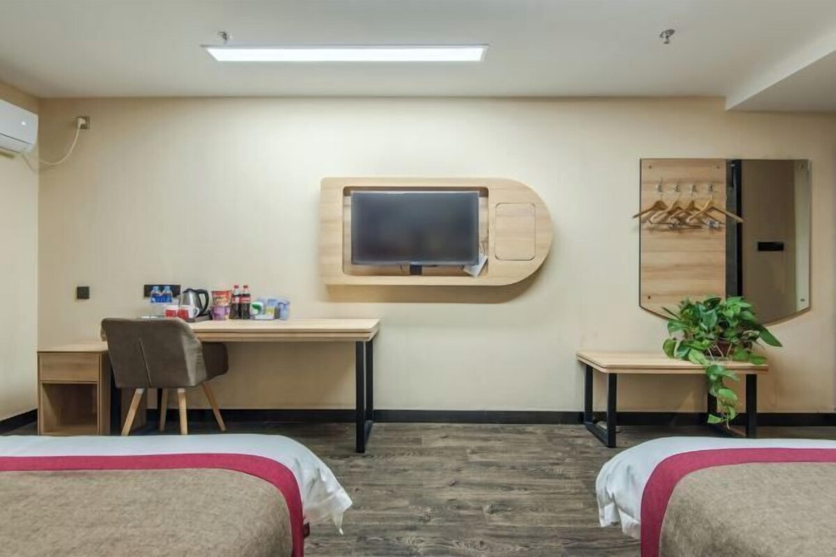 A hotel room with two beds, a desk, a TV mounted on the wall, a mirror, and a plant.