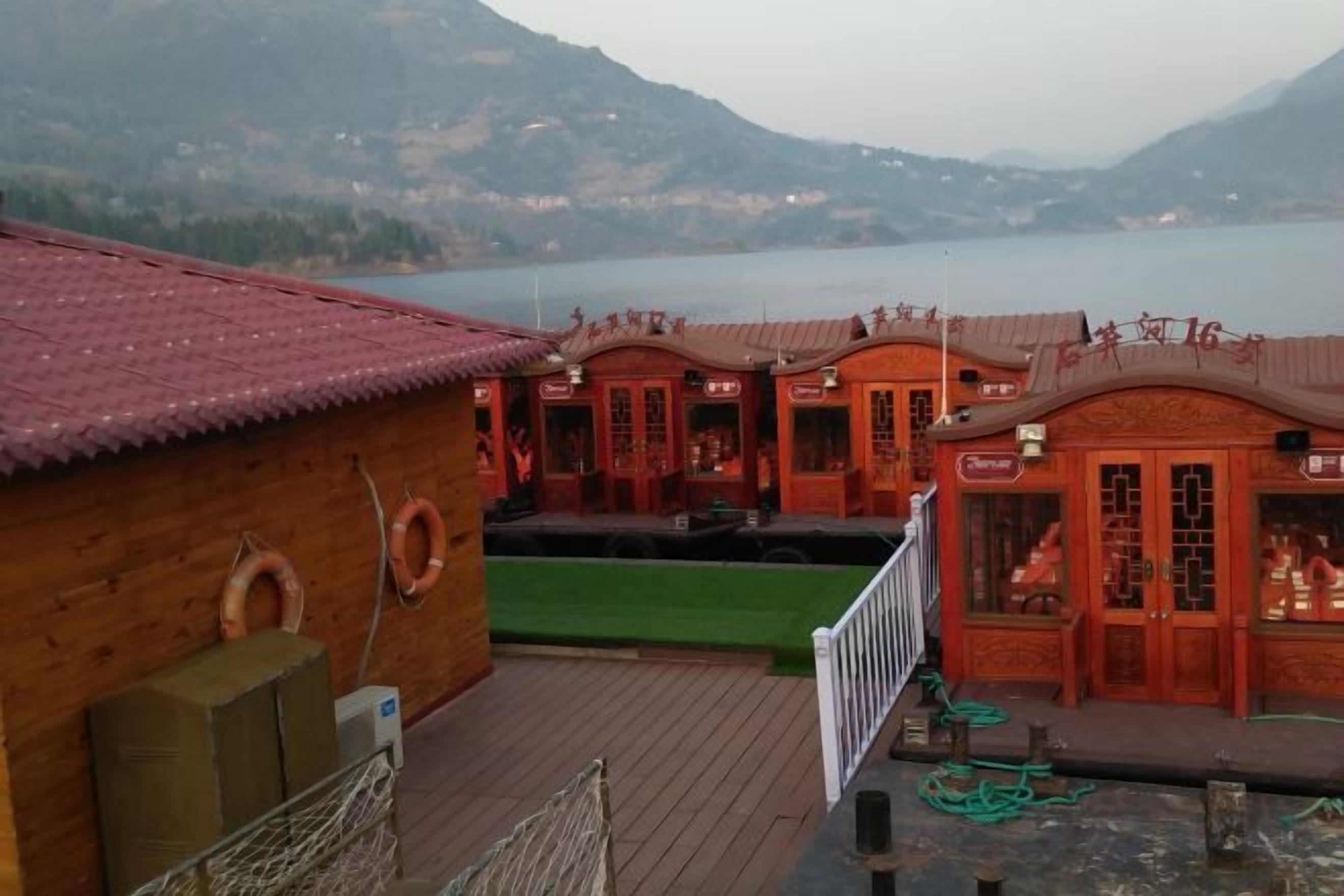 A wooden building with a red roof, a pool, and a view of a lake and mountains.