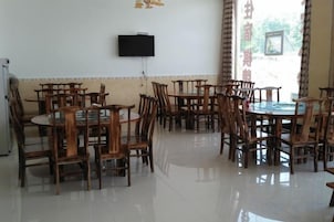 A dining area with multiple wooden tables and chairs, a flat-screen TV mounted on the wall, and a window with curtains.