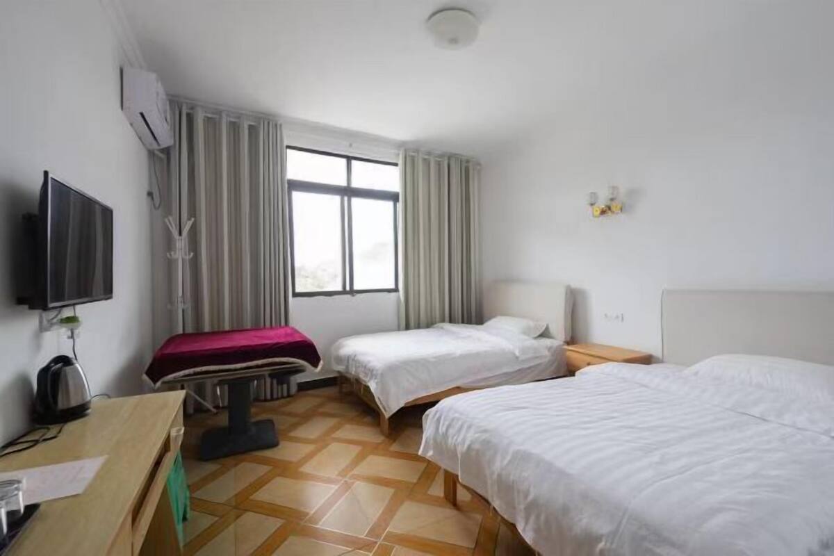 A hotel room with two beds, a desk with a kettle, a television, and a window with curtains.