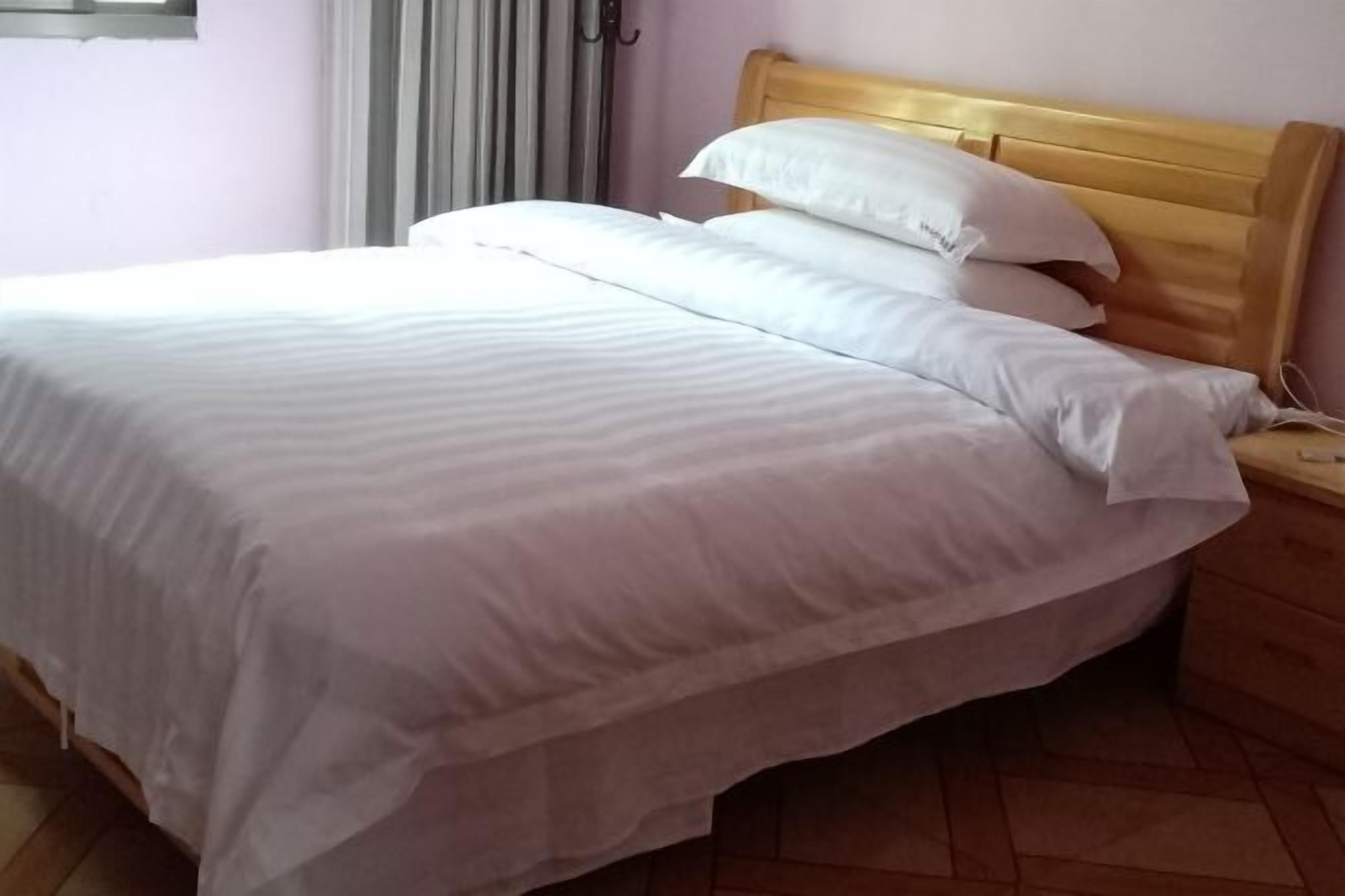 Ein ordentlich bezogenes Bett mit weißer Bettwäsche und einem Holz-Kopfteil in einem Zimmer mit Fliesenboden.