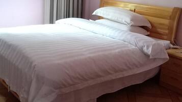 Ein ordentlich bezogenes Bett mit weißer Bettwäsche und einem Holz-Kopfteil in einem Zimmer mit Fliesenboden.