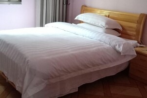 Una cama bien hecha con ropa de cama blanca y cabecera de madera en una habitación con suelo de baldosas.
