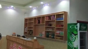 A reception area with a wooden desk, shelves with beverages, and a refrigerator.