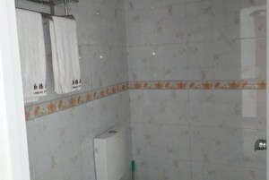 Un baño con azulejos blancos, un borde floral y un perchero con dos toallas.