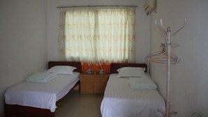A room with two single beds, a wooden nightstand, a hanging coat rack, and a window with a floral curtain. - Lianfa Guesthouse (Lingchuan)