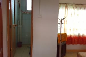 Un baño con ducha, inodoro y lavamanos. Hay una ventana con cortinas y un perchero.