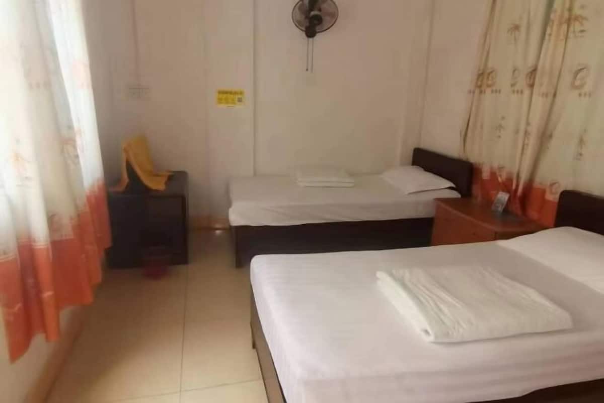 A hotel room with two beds, a bedside table, a chair, and a fan.