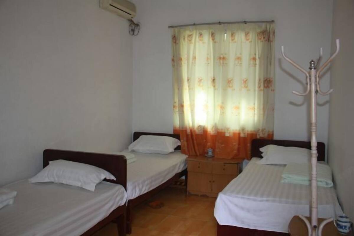 A small, simple room with two single beds, a wooden nightstand, and a coat rack.