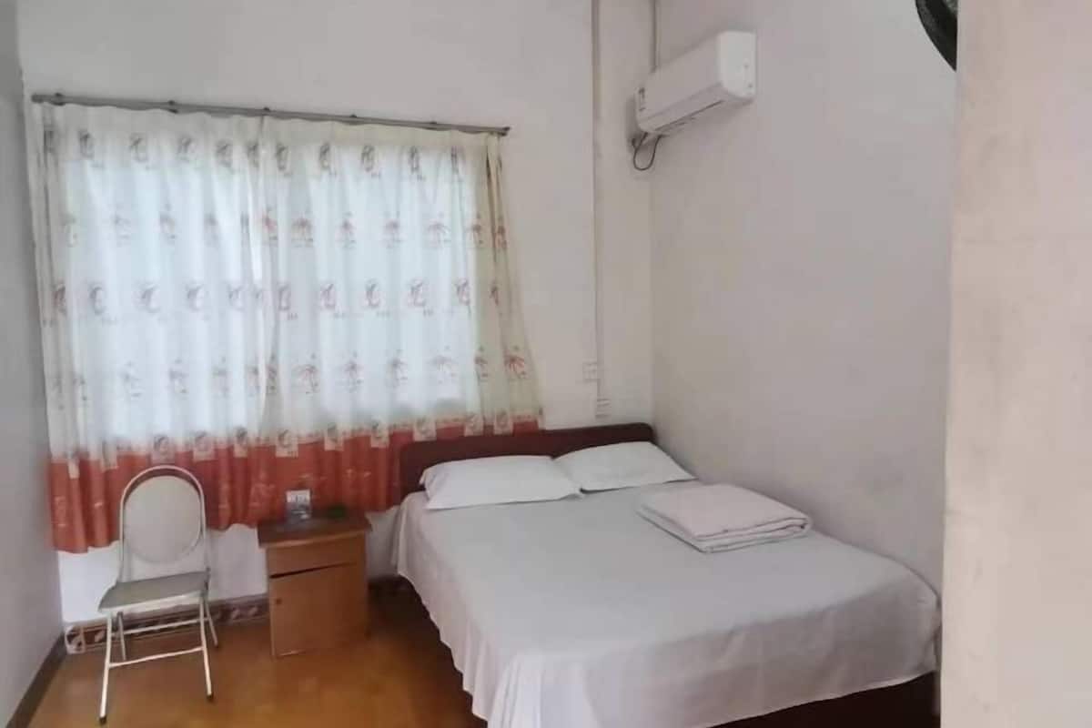 A bedroom with a bed, a chair, a nightstand, and a window with curtains.
