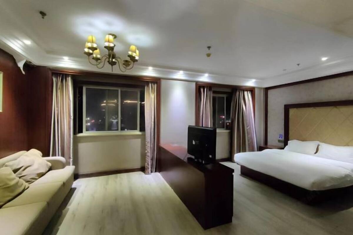 A hotel room with a bed, a sofa, a TV, and a window with curtains.