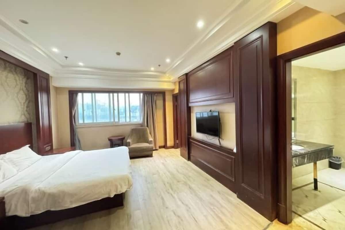 A hotel room with a bed, a TV, a chair, a window, and a bathroom.