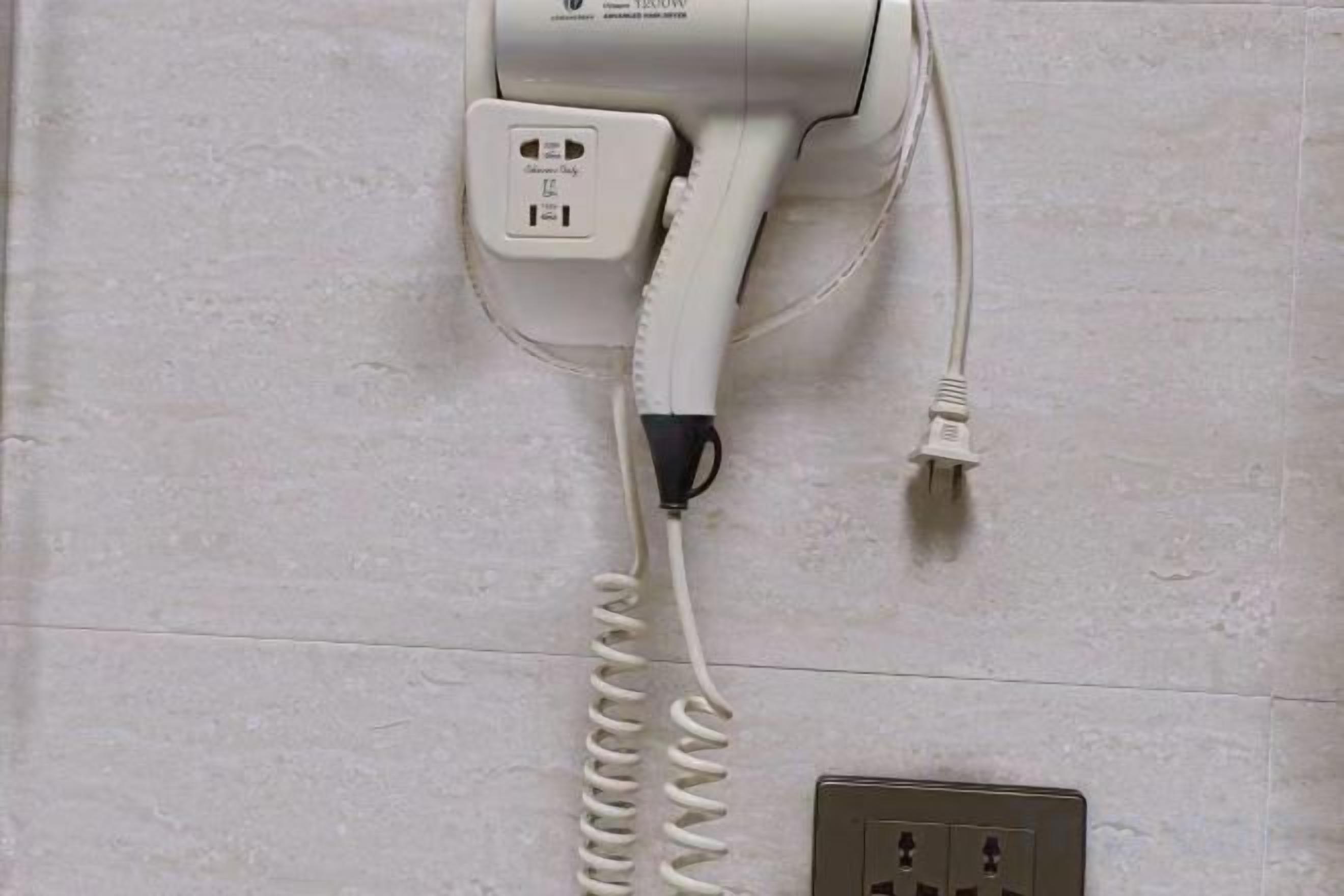 A hair dryer mounted on a wall with a power cord.