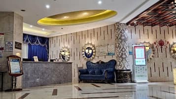 A hotel reception area with a marble floor, a reception desk, a blue sofa, and a digital information kiosk.
