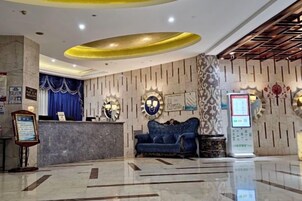 Zona de recepción de un hotel con piso de mármol, mostrador de recepción, un sofá azul y un quiosco digital informativo.