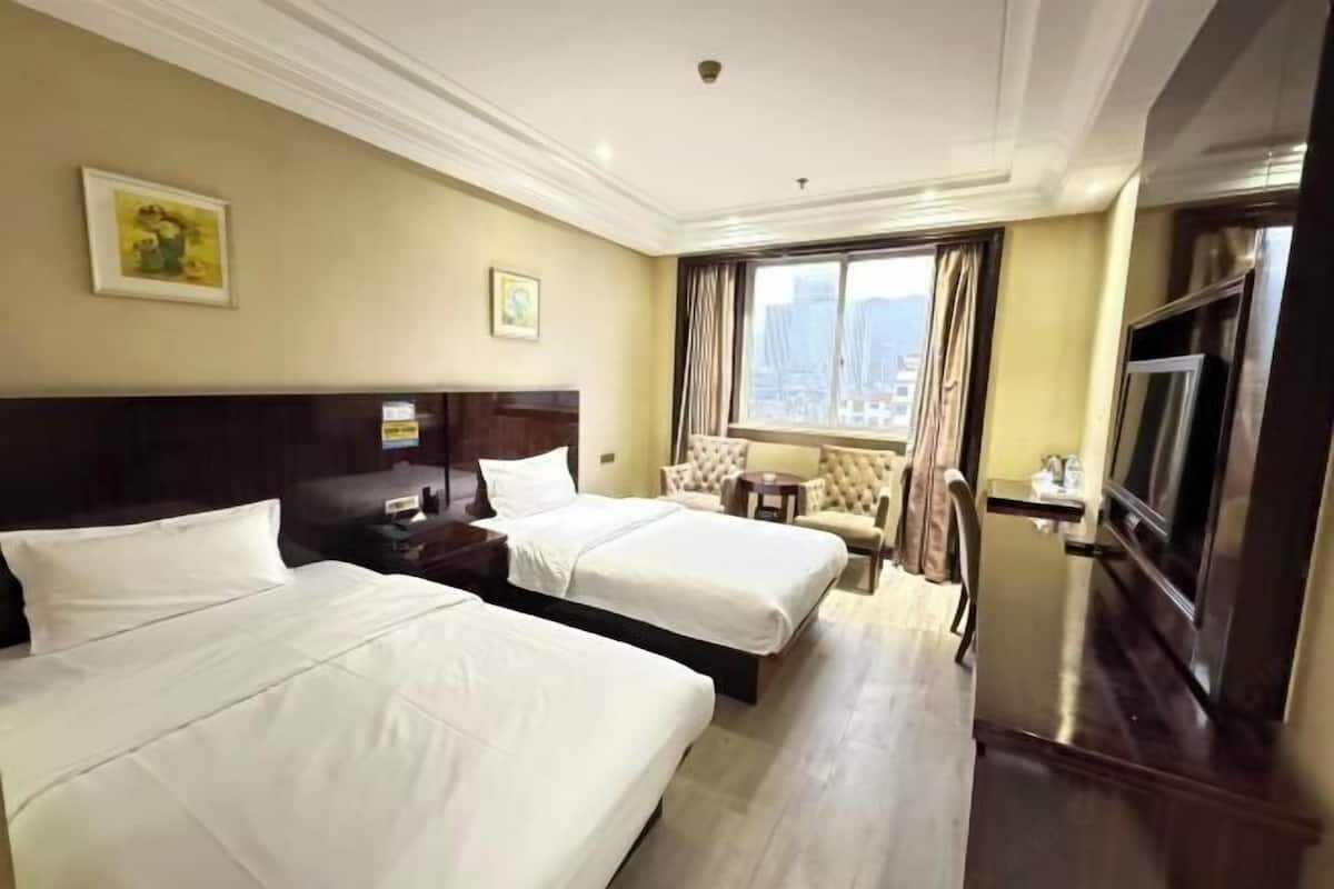 A hotel room with two beds, a TV, a window with curtains, and a city view.