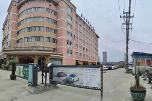 Un hotel de varios pisos con fachada curva, un cartel y un estacionamiento con coches.