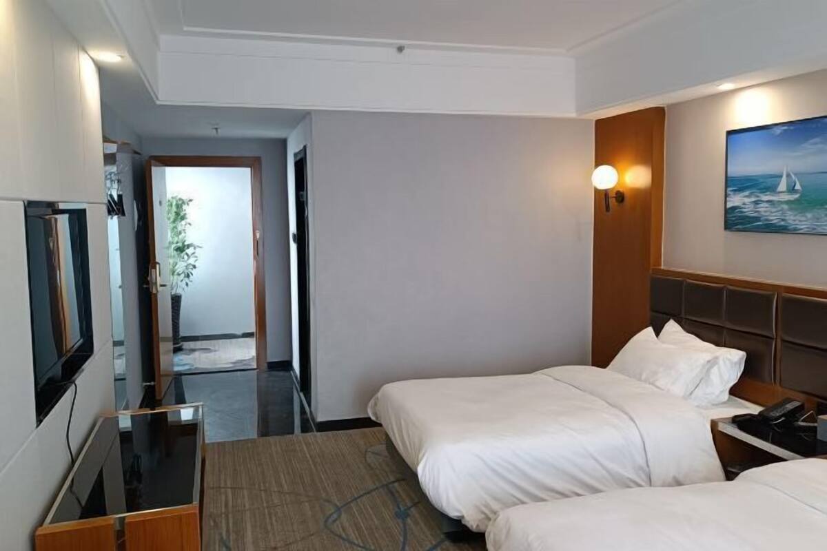 A hotel room with two beds, a TV, a desk, and a painting of a sailboat.