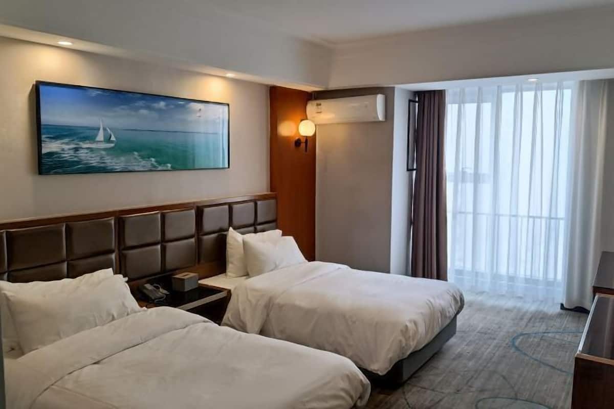 A hotel room with two beds, a painting of a sailboat, an air conditioning unit, and a view of the outdoors.