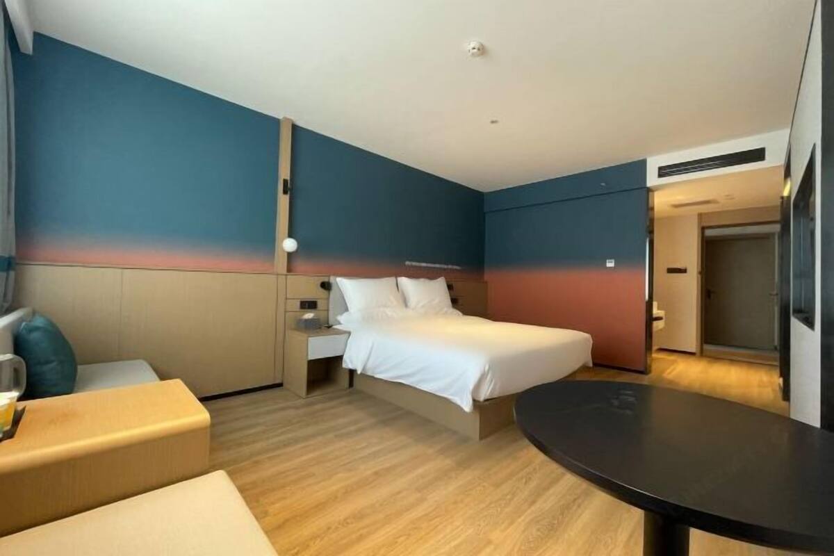 A modern hotel room with a bed, bedside tables, a sofa, and a small table.