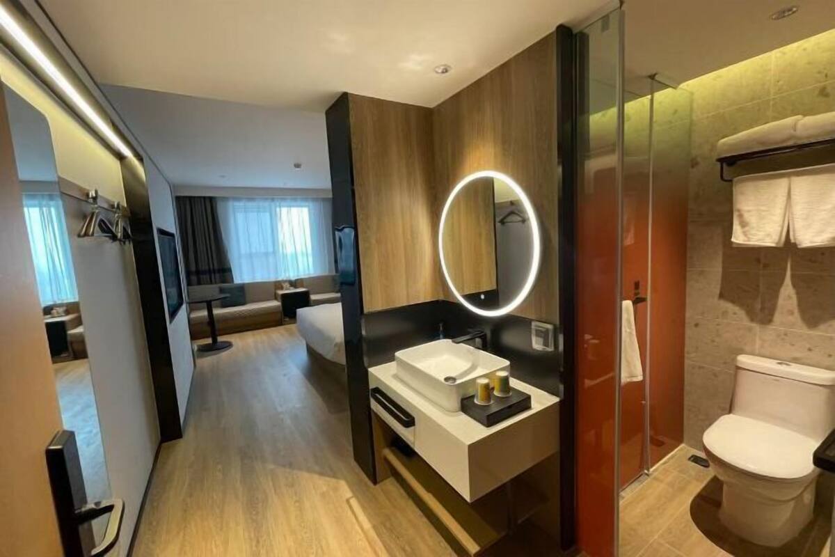 A modern hotel bathroom with a vanity, a toilet, and a glass-enclosed shower.