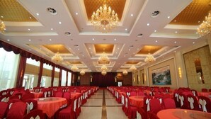 Un salón de banquetes con mesas redondas, sillas rojas, candelabros y un cuadro grande en la pared.