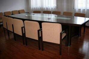 Ein Konferenzraum mit einem langen Tisch, Stühlen, Holzboden und einem Fenster mit Vorhängen.