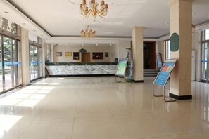 Un vestíbulo de hotel con un mostrador de recepción de mármol, un candelabro y carteles informativos.