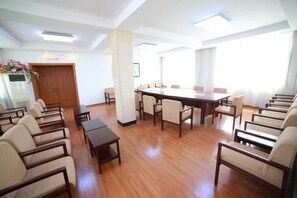 Un salón de conferencias con una larga mesa y sillas, piso de madera y ventanas amplias.