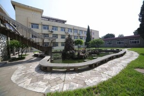 Un patio con una fuente, un sendero de piedra y un edificio con múltiples ventanas y una escalera.
