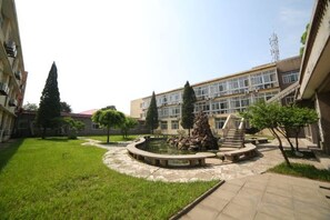 Un patio central con una fuente, rodeado de vegetación y un edificio de varios pisos y ventanas.