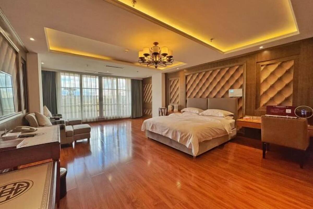 A hotel room with a large bed, a desk, a chair, and a view of the outdoors.