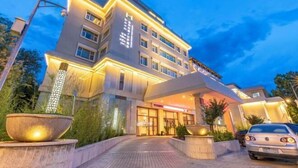 A multi-story hotel with a modern design, featuring a prominent entrance with a covered walkway and large planters. - Himalaya Lhasa Hotel (Lhasa)