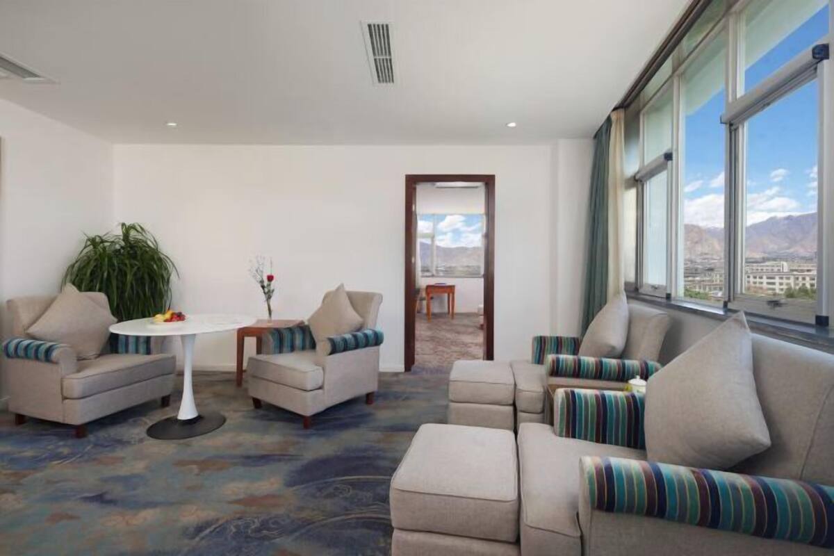 A modern hotel room with a large window, a sofa set, a small table, and a potted plant.