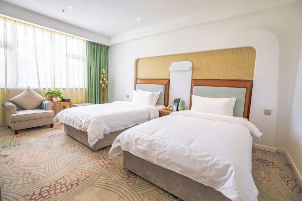 A hotel room with two beds, a sofa, a nightstand, and a window with curtains.