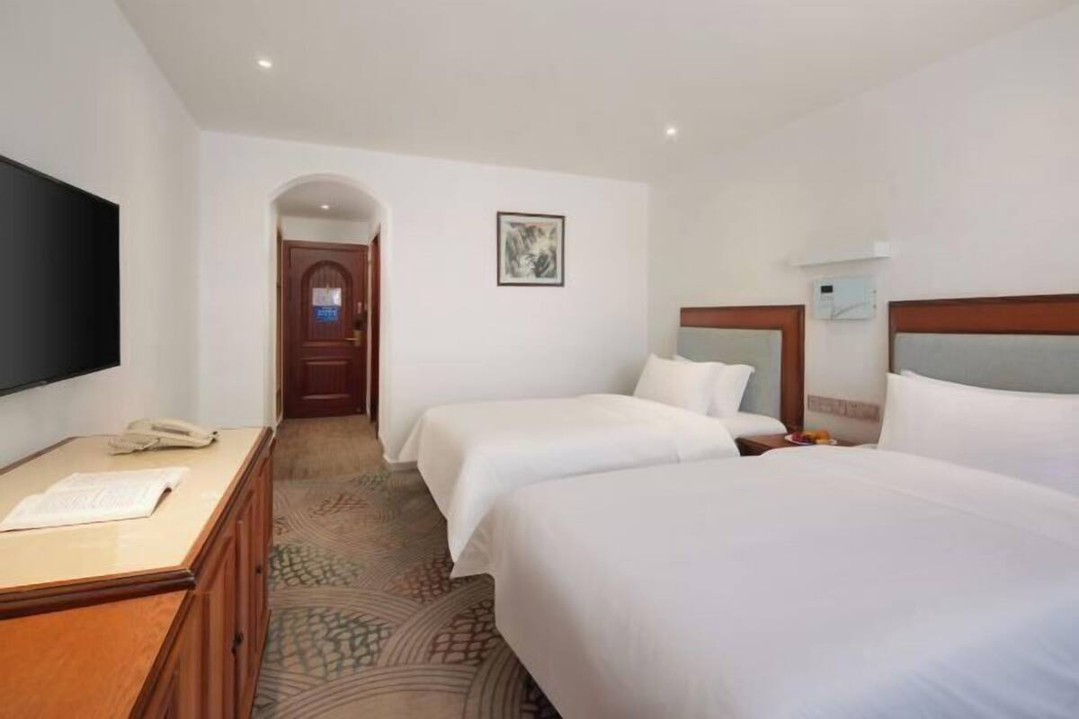 A hotel room with two beds, a desk with a telephone, a flat-screen TV, and a framed picture on the wall.