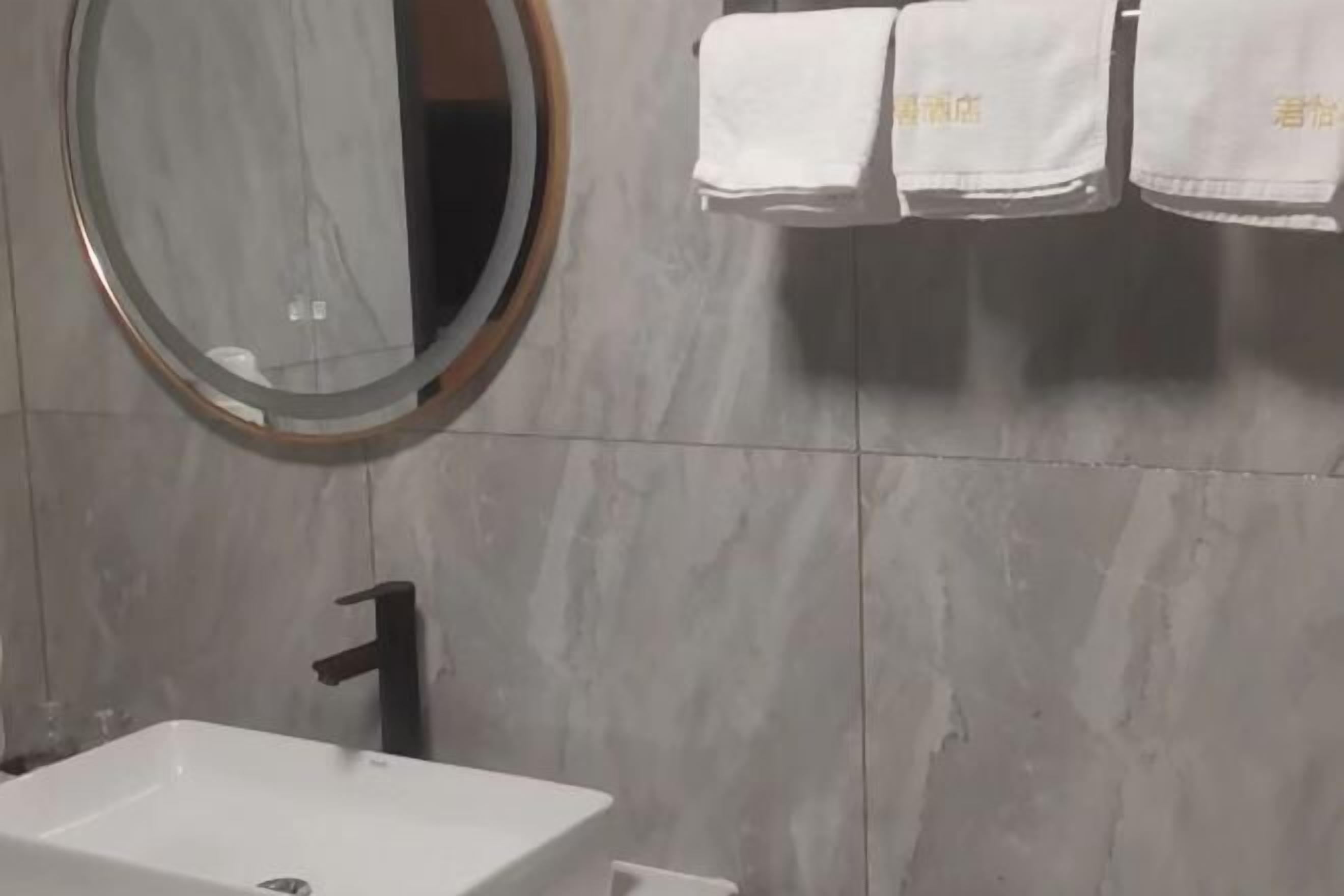A bathroom with a round mirror, a white sink, a black faucet, and a towel rack with white towels.