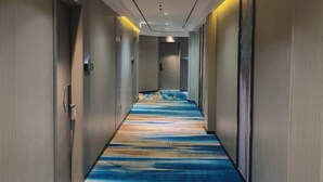 Un couloir d’hôtel avec un tapis à motifs, des murs en bois et un éclairage encastré.