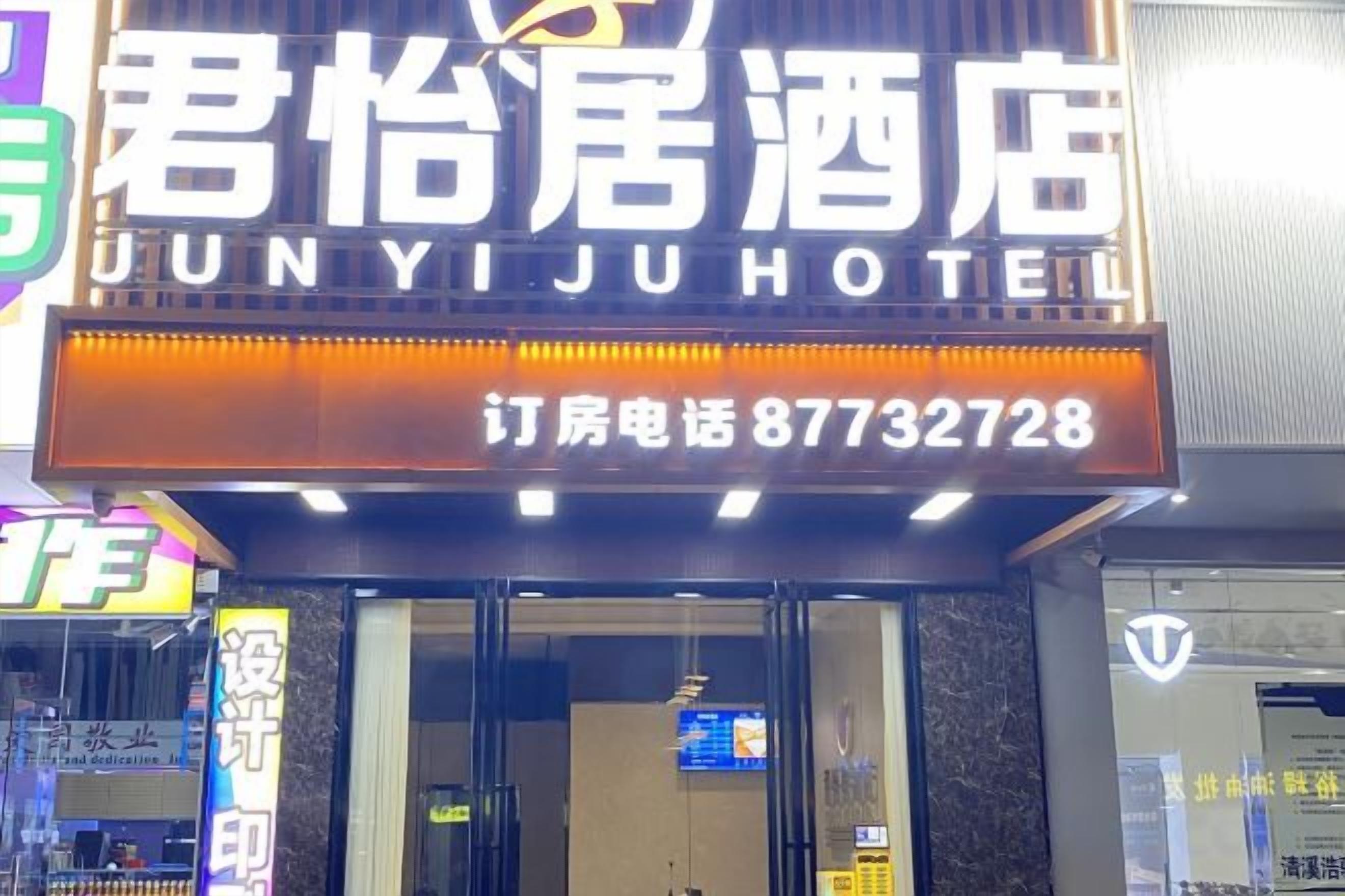 L’entrée d’un hôtel, avec une enseigne indiquant le nom « JUNYIJU HOTEL » et un numéro de téléphone.