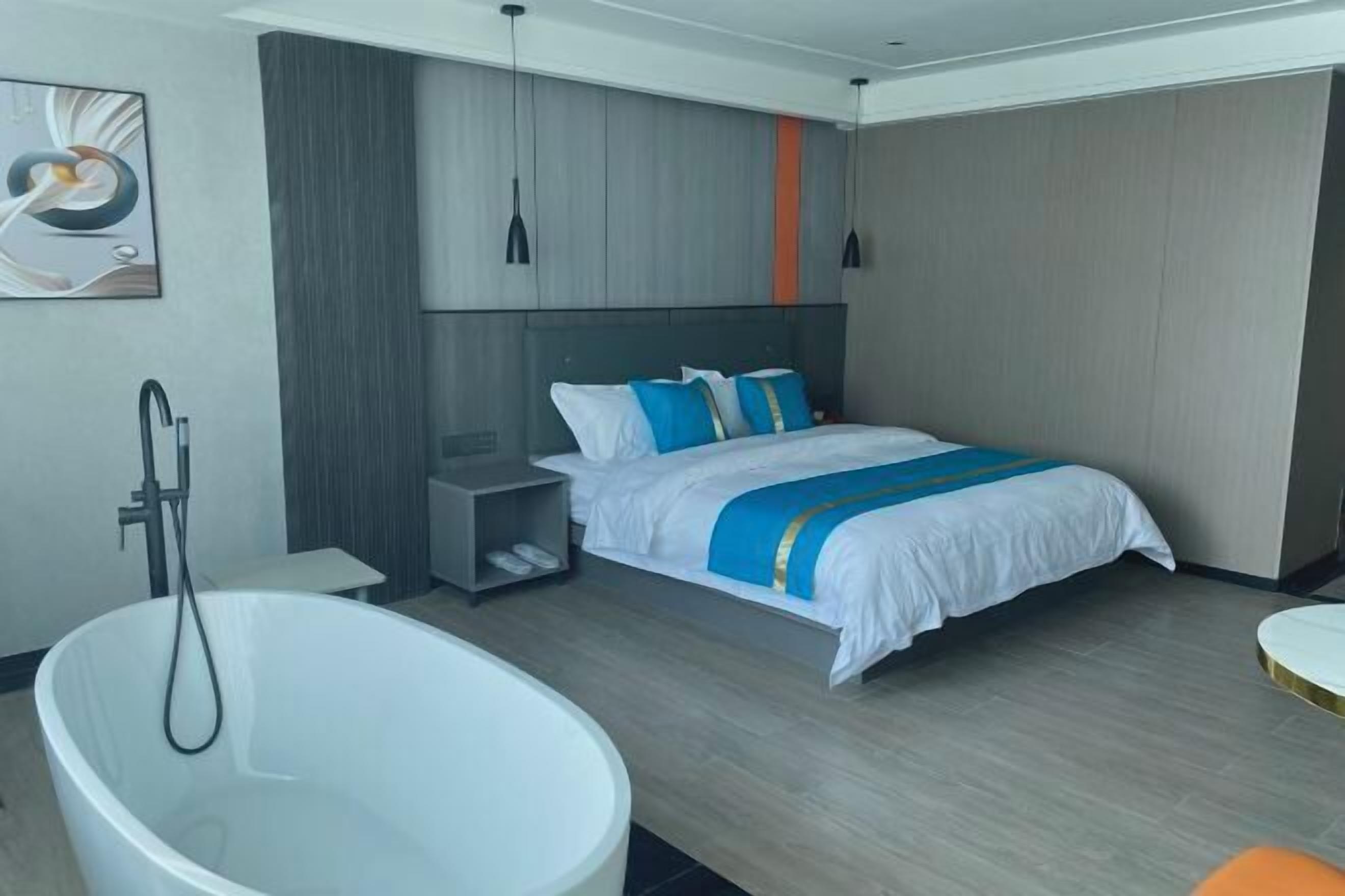 Quarto de hotel moderno com uma cama grande, uma banheira e uma mesinha de cabeceira.