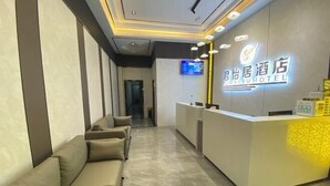 Un espace d’accueil d’hôtel au design moderne, comprenant un comptoir d’accueil, un coin salon avec des canapés et un téléviseur à écran plat fixé au mur.