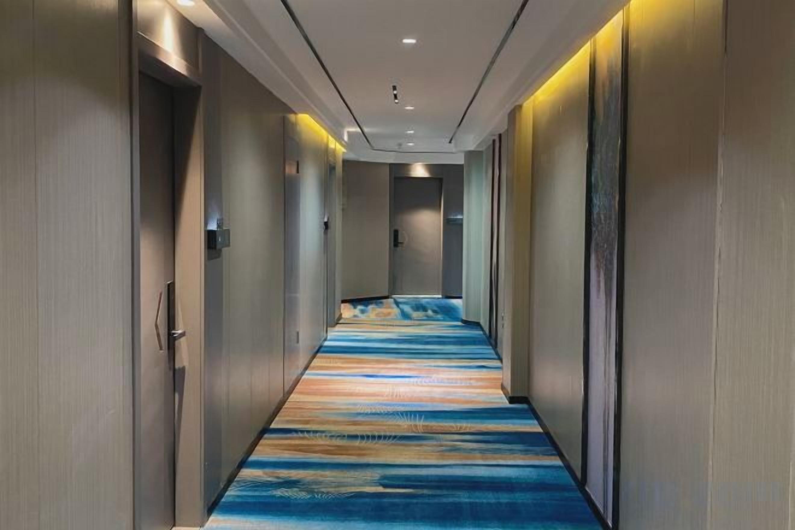 Un couloir d’hôtel avec un tapis à motifs, des portes des deux côtés et un éclairage encastré.