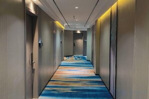 Pasillo de hotel con alfombra estampada, puertas a ambos lados e iluminación empotrada.