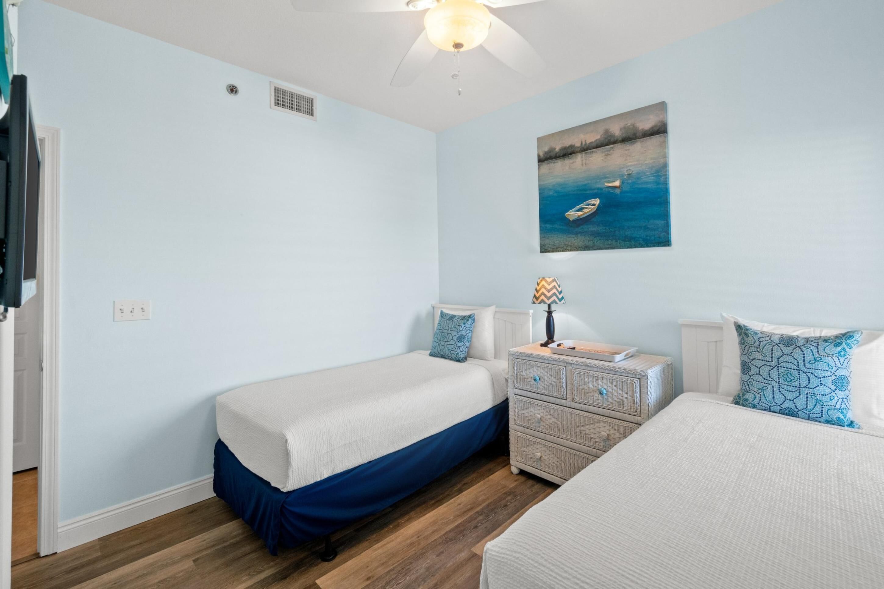 A bedroom with two beds, a nightstand, a ceiling fan, and a painting of a boat on water.