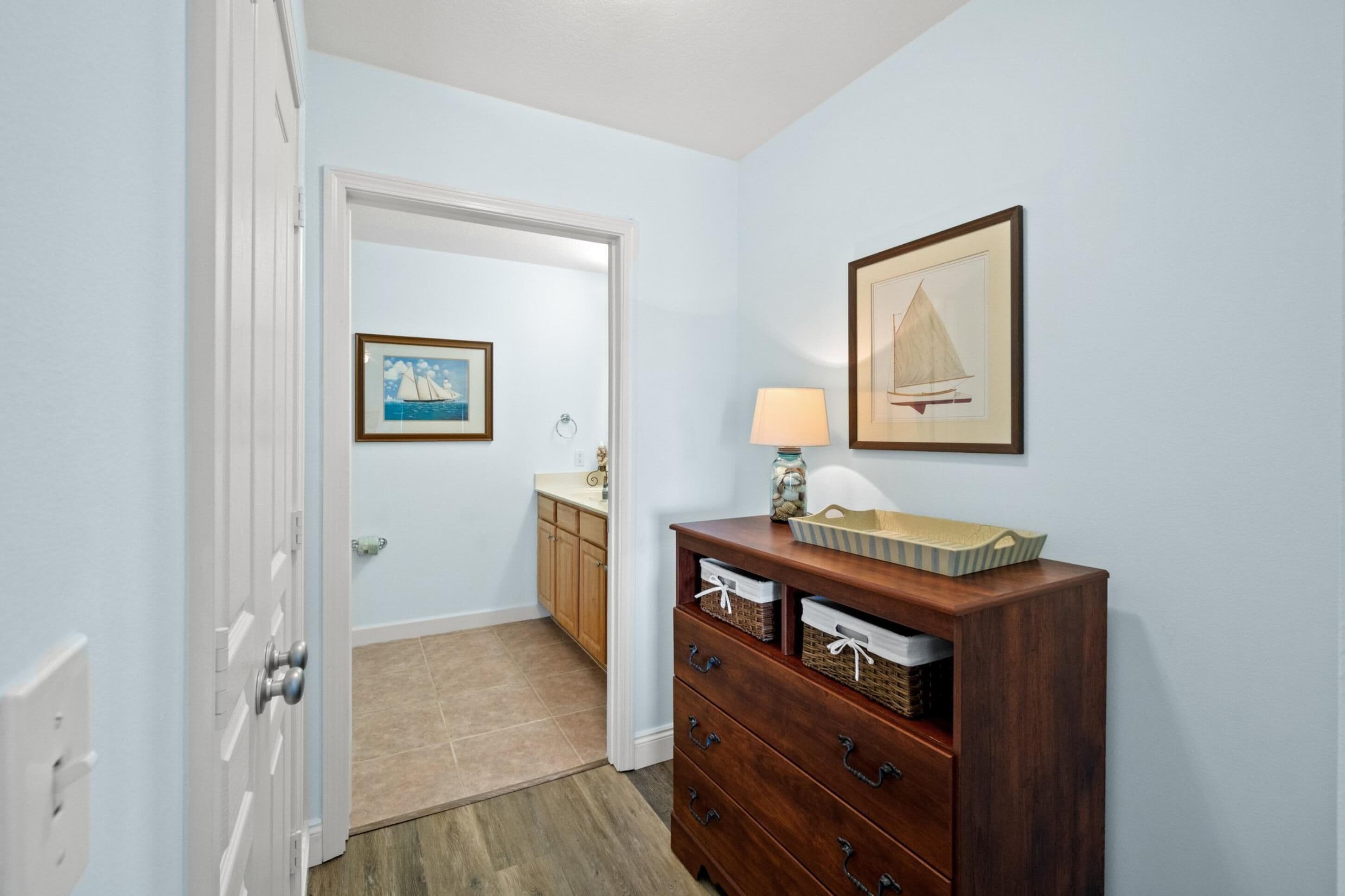 A hallway with a wooden dresser, a framed picture of a sailboat, and a door leading to a bathroom.