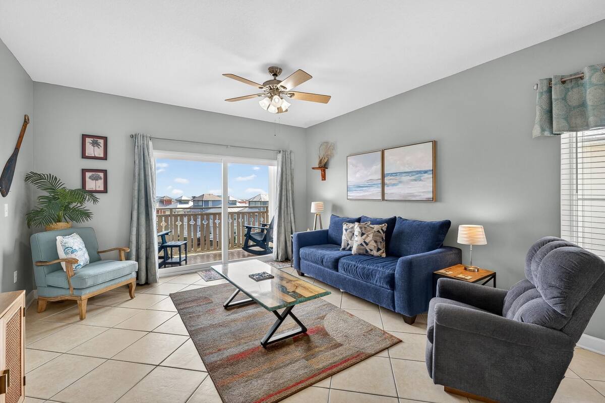 A living room with a blue sofa, a grey armchair, a glass coffee table, and a ceiling fan.