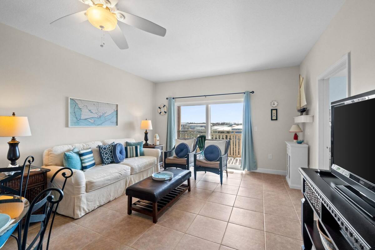 A living room with a sofa, chairs, a coffee table, a TV, and a balcony with curtains.