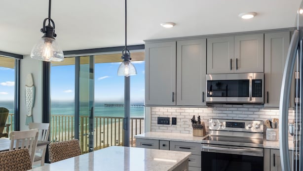 A modern kitchen with a large island, stainless steel appliances, and a view of the ocean.