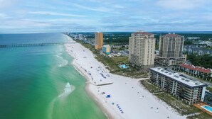 A coastal cityscape with a wide sandy beach, high-rise buildings, and a long pier extending into the ocean.